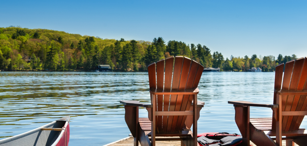 Tranquil view of Muskoka lake from two empty Adirondack chairs, highlighting the authentic experiences offered by Jayne's Luxury Rentals