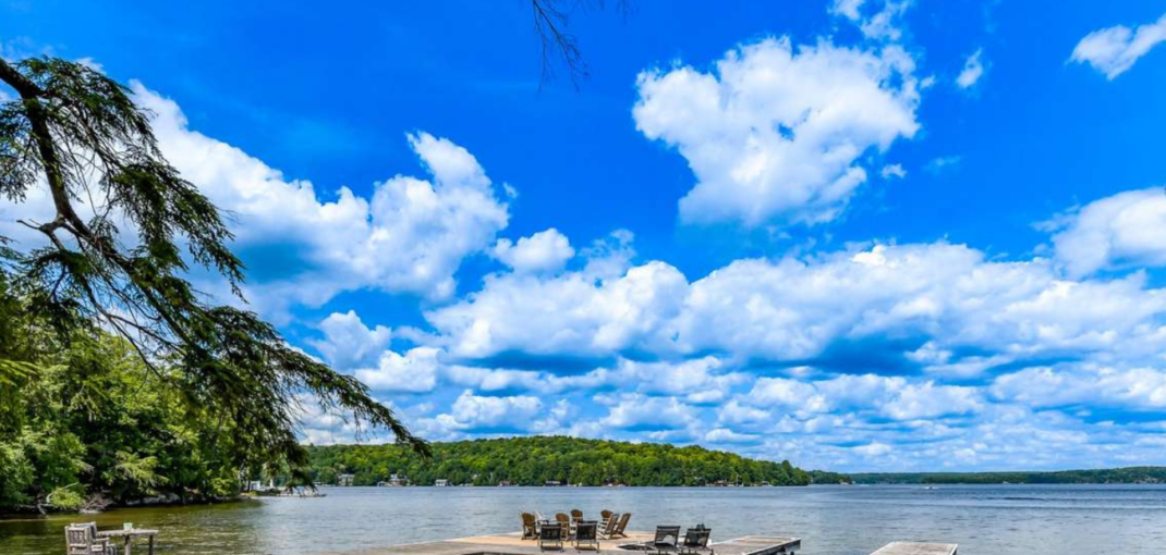 Panoramic view of a peaceful lakefront with seating arranged on the dock, exemplifying ideal summer cottage settings - Jayne's Luxury Rentals