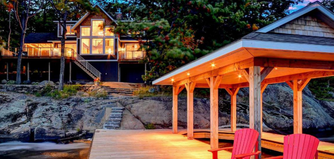 Twilight view of Bella Muskoka cottage with illuminated interiors and waterside gazebo in Port Carling, Ontario - featured in 6 Hot New 2019 Cottages blog - Jayne's Luxury Rentals