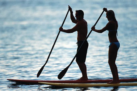 Silhouettes of two people stand-up paddleboarding at dusk, a serene activity offered by Jayne's Luxury Rentals