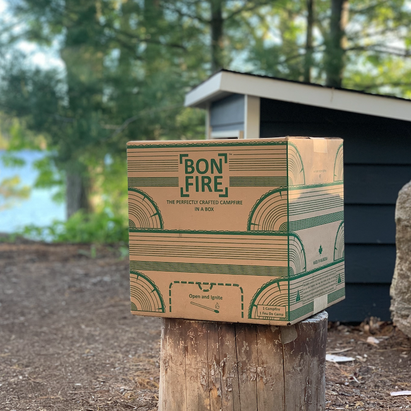 Bon Fire campfire box provided by Jayne's Luxury Rentals, set on a stump with a blurred lakeside cabin background, enhancing outdoor guest experiences