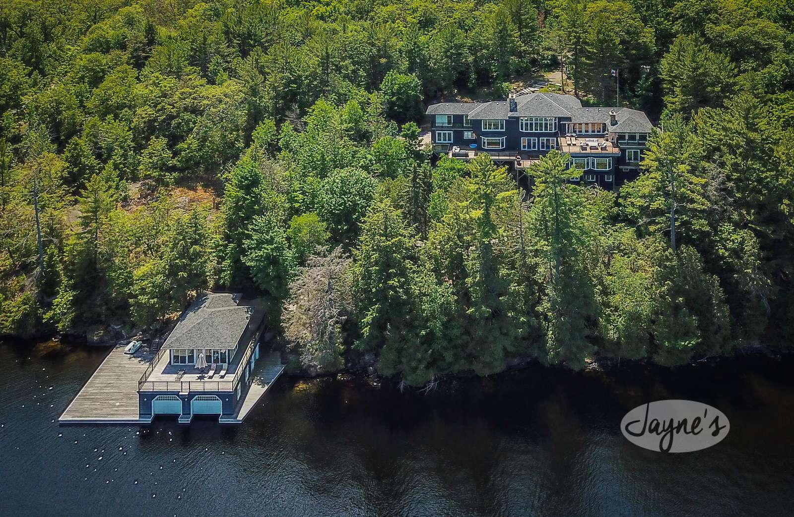 King Arthur's Court in Port Carling - Jayne's Luxurious Rentals | Aerial view of a grand lakeside property with a spacious boathouse