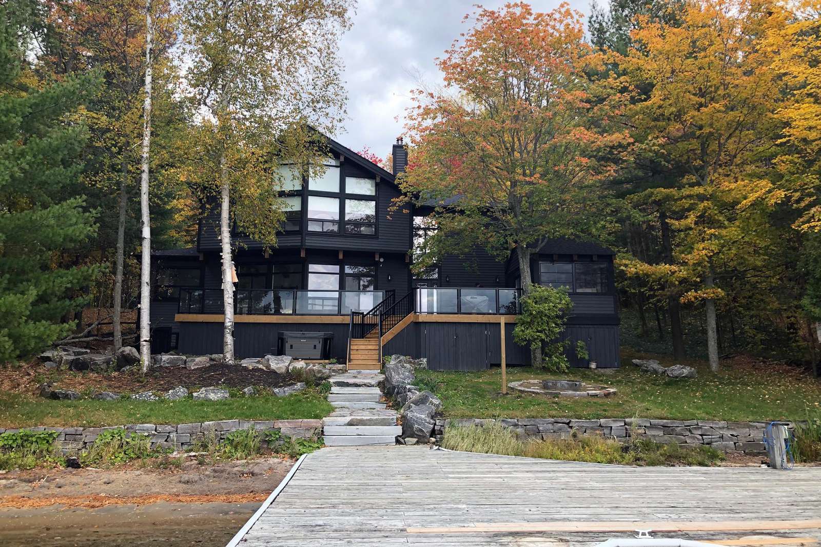 Claremont house in Port Carling - Jayne's Luxurious Rentals | Modern black facade with autumnal trees and a wooden dock
