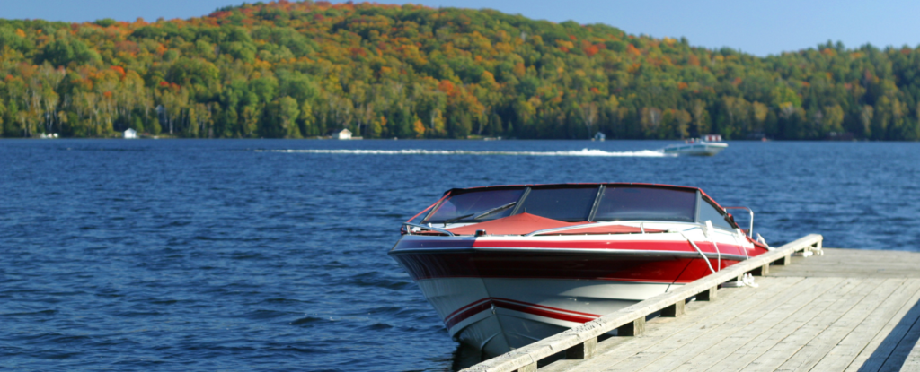 A sleek motorboat docked on a serene Muskoka lake with autumn foliage in the background, available for use with Jayne's Luxury Rentals.