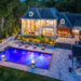 Illuminated luxury poolside villa at dusk in Innisfil by Jayne's Luxury Rentals, with a glowing blue pool and fire features.