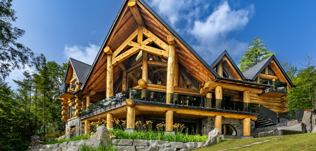 Majestic log cabin architecture of Muskoka Bay Lodge amidst lush greenery at Lake Muskoka - Jayne's Luxury Rentals.