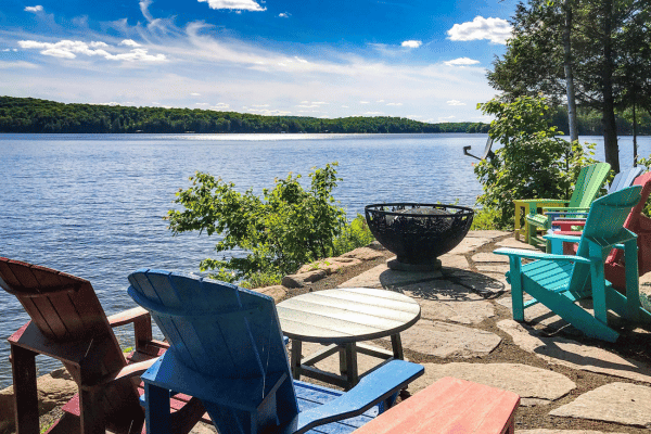 Colorful Adirondack chairs by the lake with a fire bowl offer a perfect relaxation spot at Jayne's Luxurious Rentals