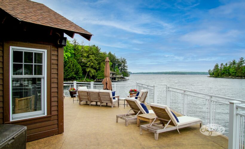 Expansive lakefront deck at Summer Breeze, a luxury Muskoka rental, featuring lounge chairs and vibrant flower pots - Jayne's Luxury Rentals.